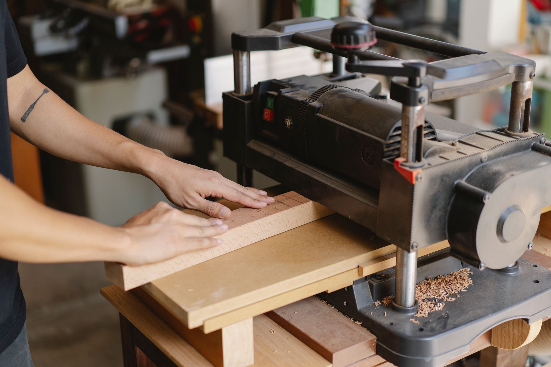 Hands guiding hardwood through a woodworking planer